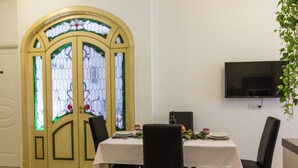 A dining area with a table set for two, a television mounted on the wall, and a stained glass door.