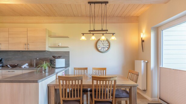 Uma cozinha moderna com armários de madeira, uma ilha central e uma área de jantar com quatro cadeiras e uma mesa de madeira.