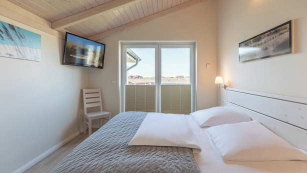 A bedroom with a bed, a chair, a TV, and a window with blinds.