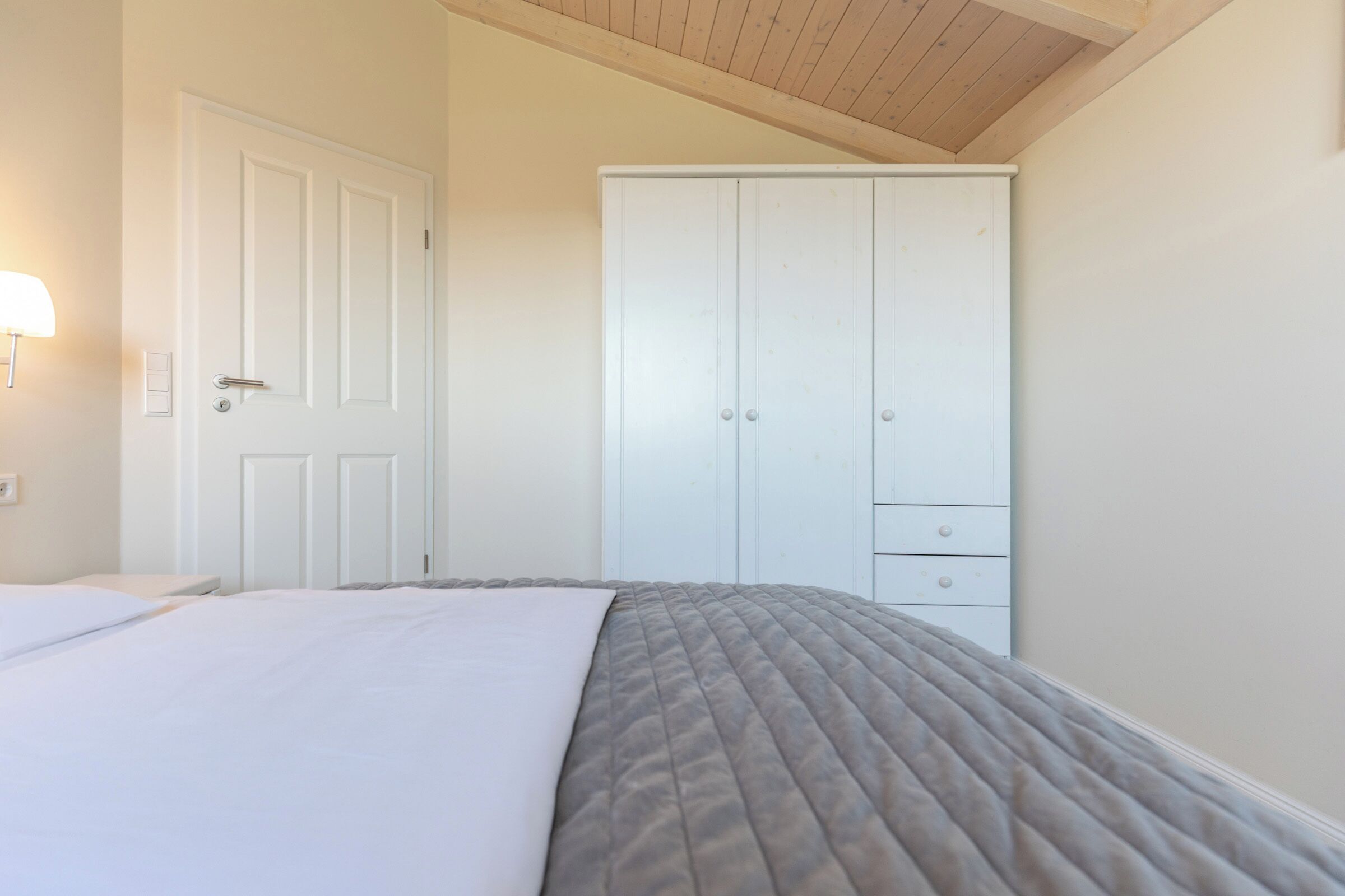 A bedroom with a bed, a wardrobe, and a wall-mounted light fixture.