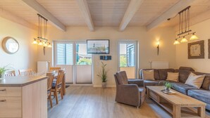 A spacious living room with a wooden ceiling, a sofa set, a coffee table, and a TV mounted on the wall.