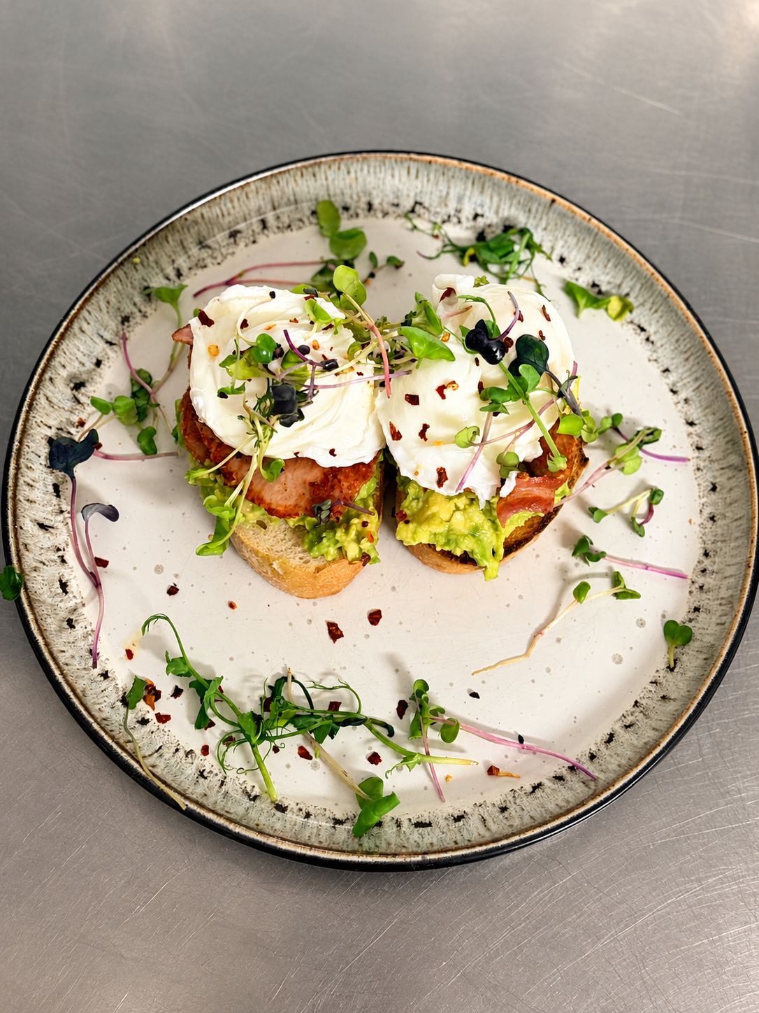 Une assiette contenant deux sandwichs ouverts garnis d’avocat, de crème et de verdure, le tout présenté sur une assiette en céramique à texture particulière.