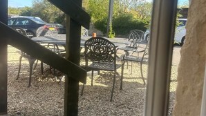 A view through a window of a patio area with outdoor seating, gravel ground, and a wooden pergola structure. - The White Hart (Melksham)