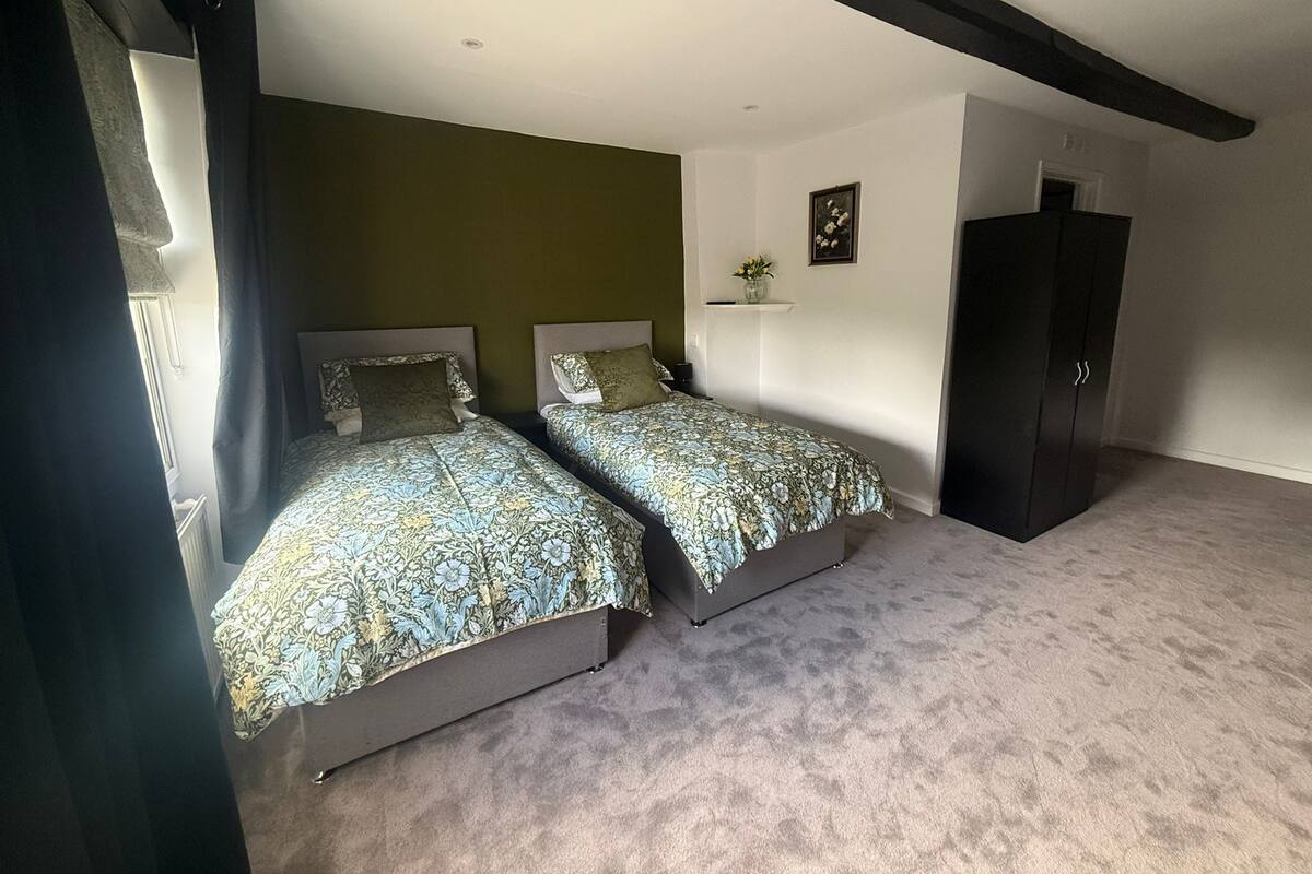 A bedroom with two beds, a dark wardrobe, a small shelf with a vase, and a framed picture on the wall.