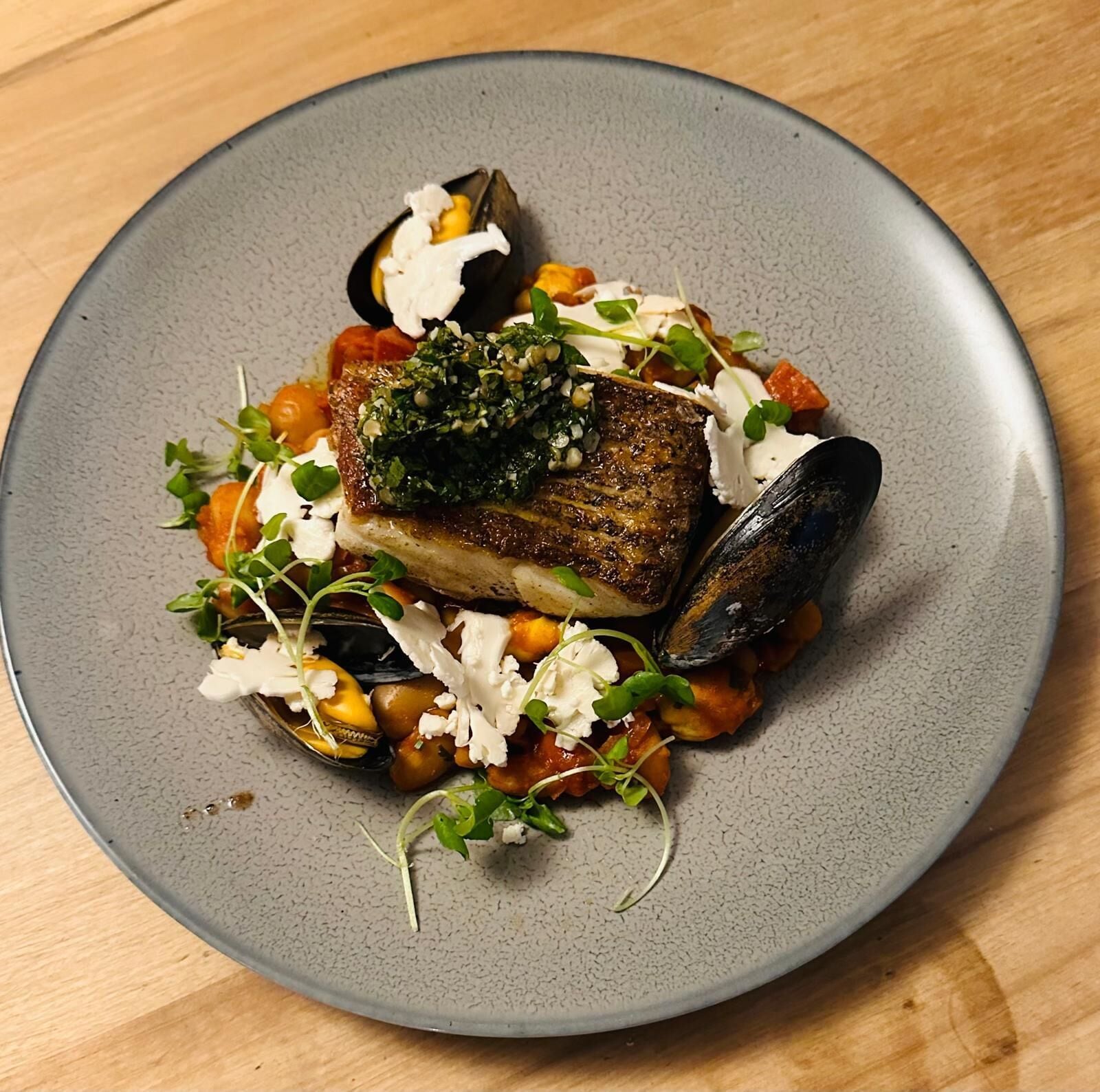 A plate of food with a piece of fish, mussels, and vegetables.