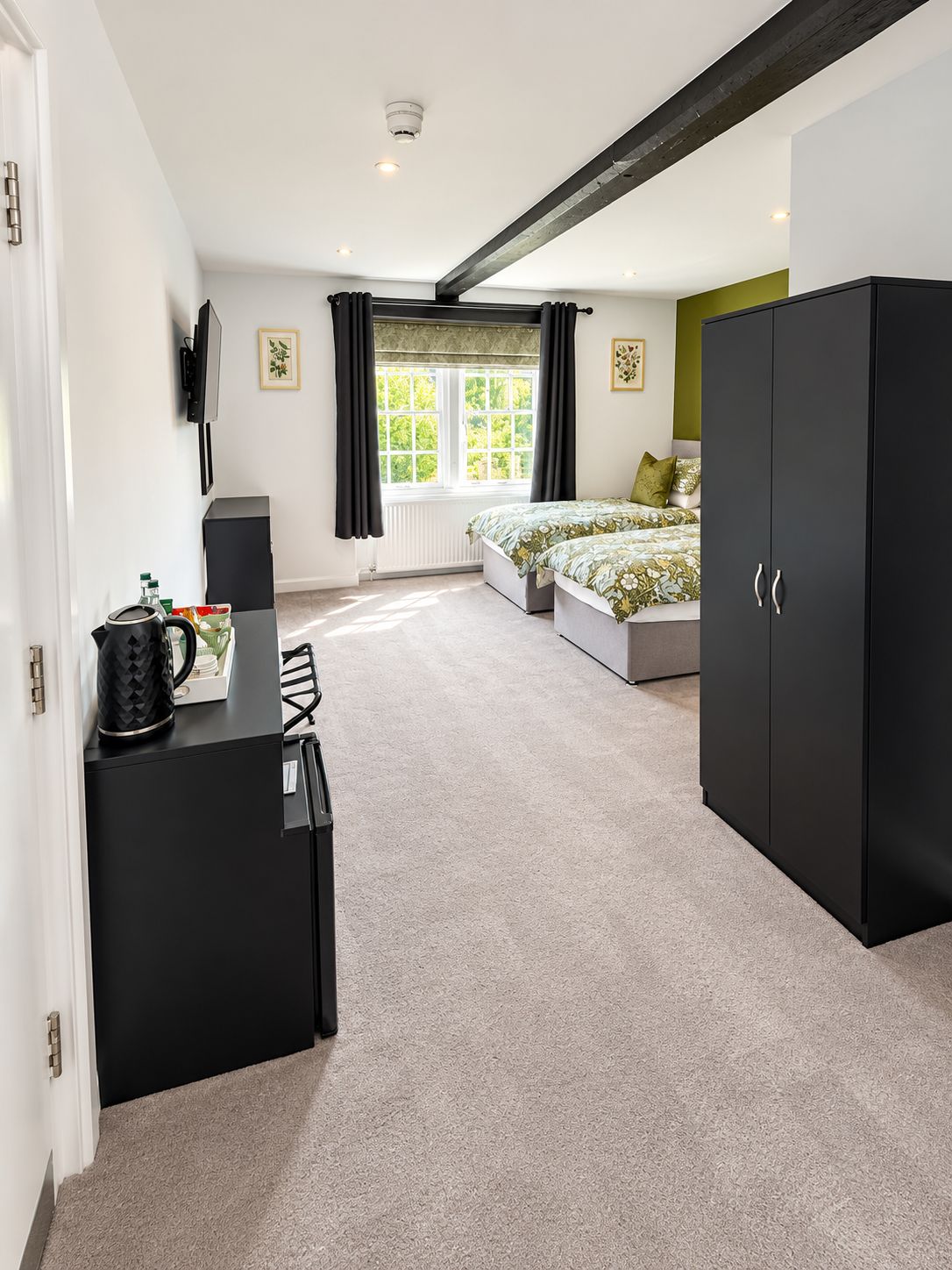 A bedroom with a bed, a wardrobe, a desk with a kettle, and a radiator.