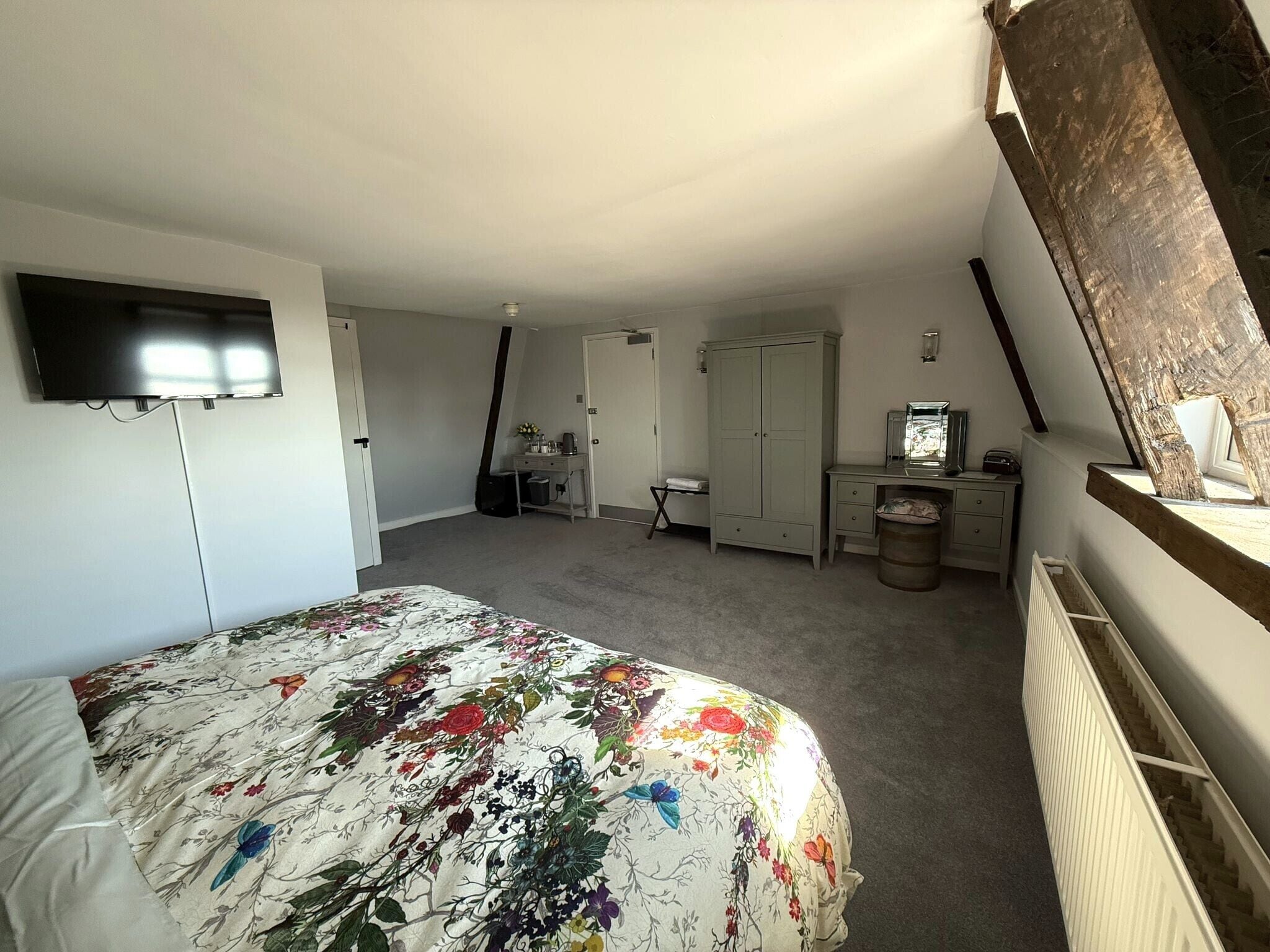 A bedroom with a bed, a dresser, a desk, a wardrobe, and a television.