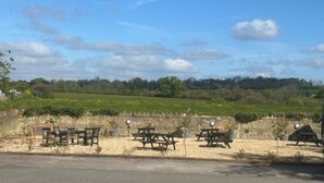A picnic area with tables and benches, a stone wall, and a view of a green field and trees in the background. - The White Hart (Melksham)
