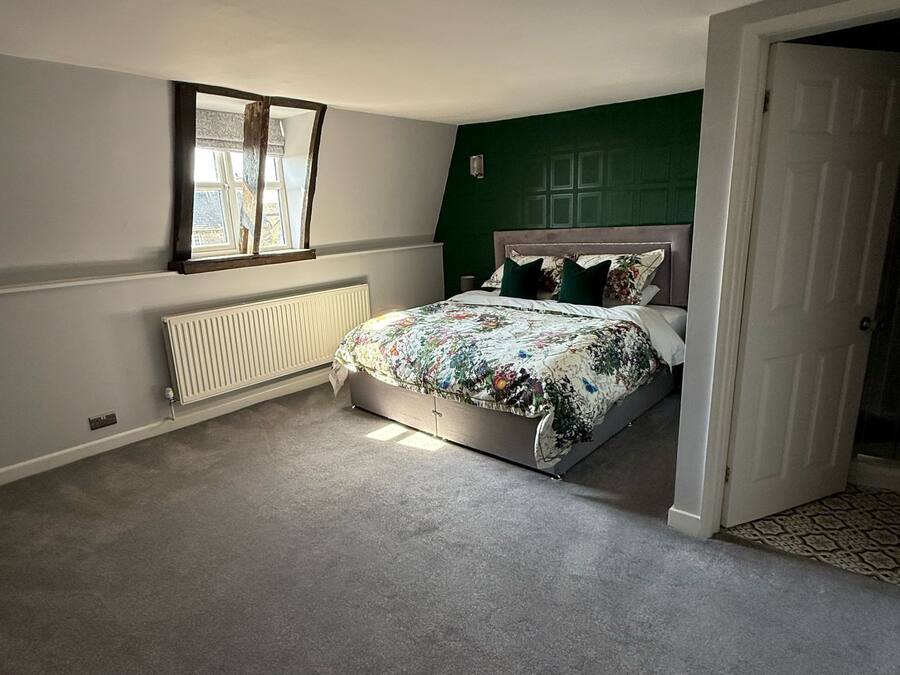 A bedroom with a bed, a radiator, a window, and a door.