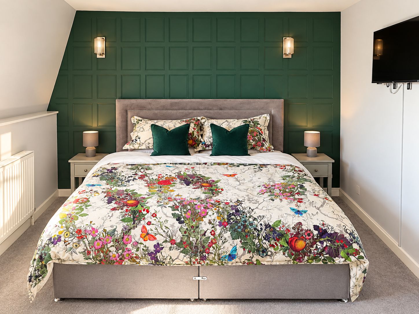Une chambre à coucher avec une couvre-lit à motifs floraux, deux lampes de chevet, un téléviseur et un mur d’accent de couleur verte.
