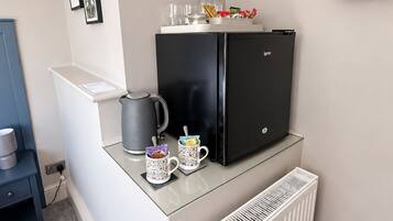 Eine kleine Küchenzeile mit einem schwarzen Kühlschrank, einer Kaffeemaschine, zwei Tassen und einem Wasserkocher auf einer Arbeitsplatte.