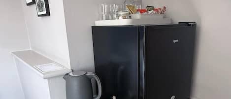 A compact kitchenette with a black refrigerator, a kettle, and two mugs on a countertop.