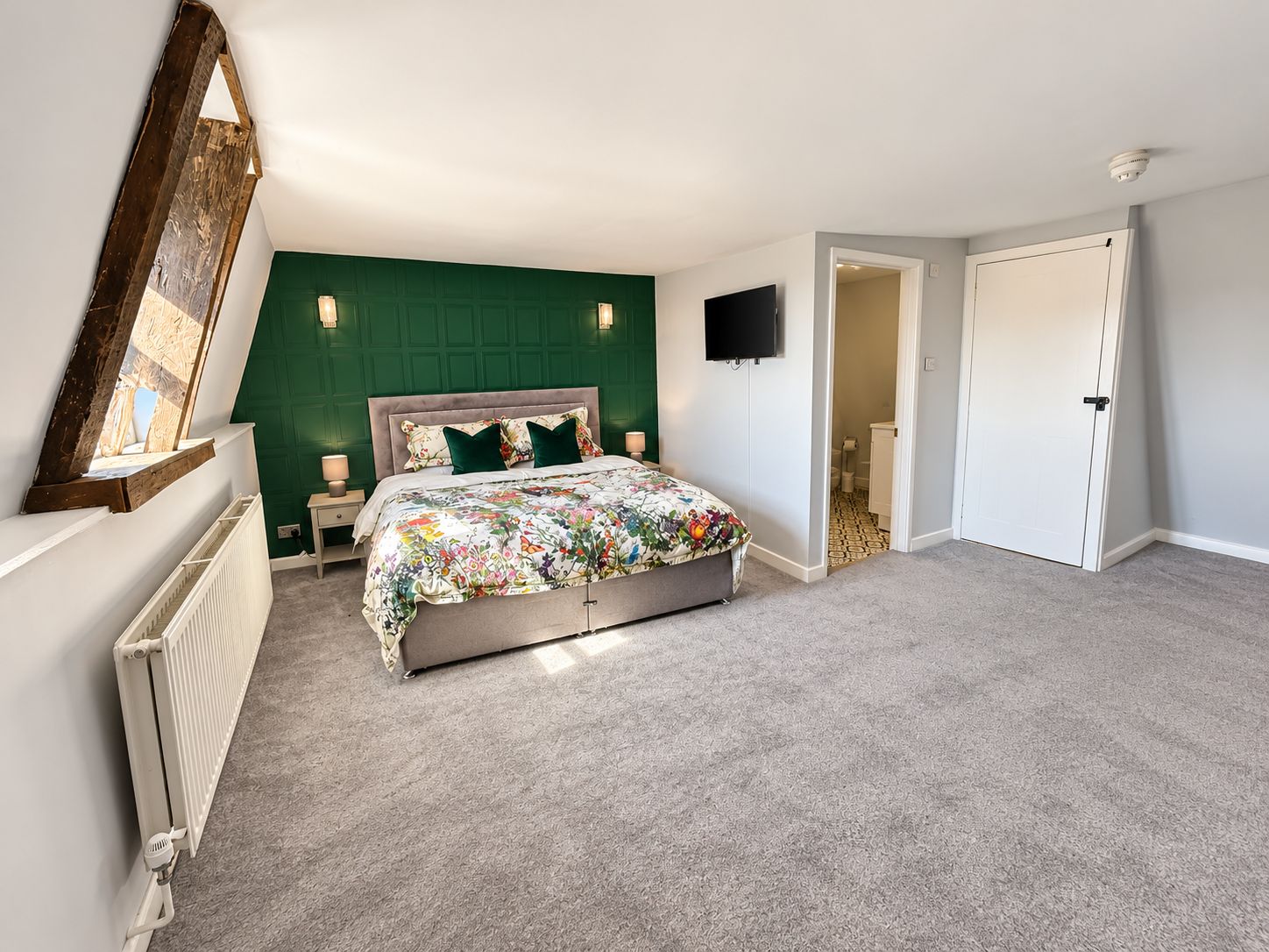 Un dormitorio con cama, televisor, puerta y radiador.