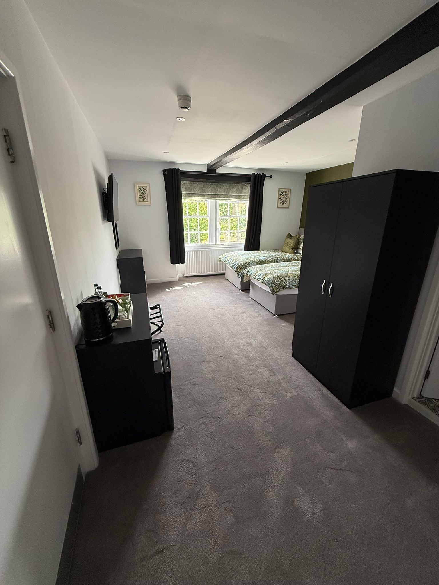 Une chambre à coucher comprenant un lit, une armoire, un bureau avec une bouilloire, un radiateur et une fenêtre avec des rideaux.