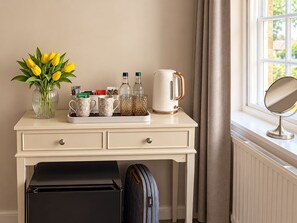 A hotel room with a desk, a vase of yellow flowers, a tray with mugs, a kettle, and a suitcase. - The White Hart (Melksham)