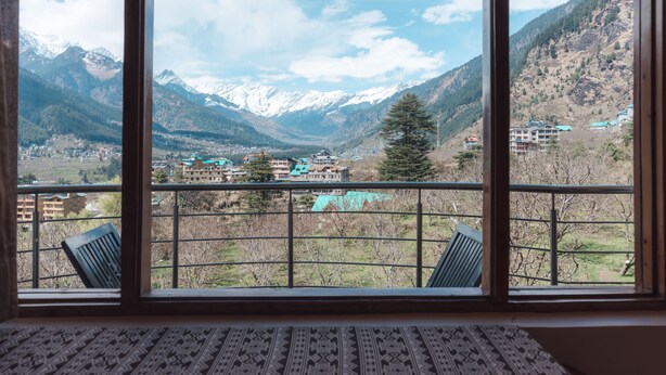 Une pièce dotée d’une grande fenêtre donnant sur un paysage montagneux, d’un tapis à motifs et de deux fauteuils.