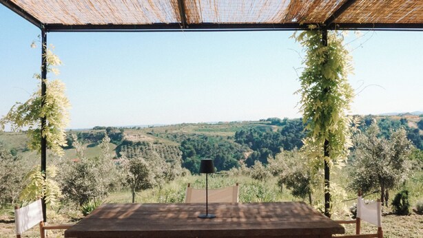 An outdoor wooden table and chairs under a bamboo roof, overlooking a hilly landscape. - Mondomini Panoramic Cottage, stunning view on sea, hills and 8500 olive trees (Marche)