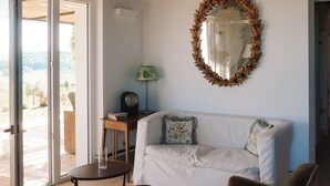 A living room with a white sofa, a brown armchair, a small table, and a mirror on the wall. - Mondomini Panoramic Cottage, stunning view on sea, hills and 8500 olive trees (Marche)