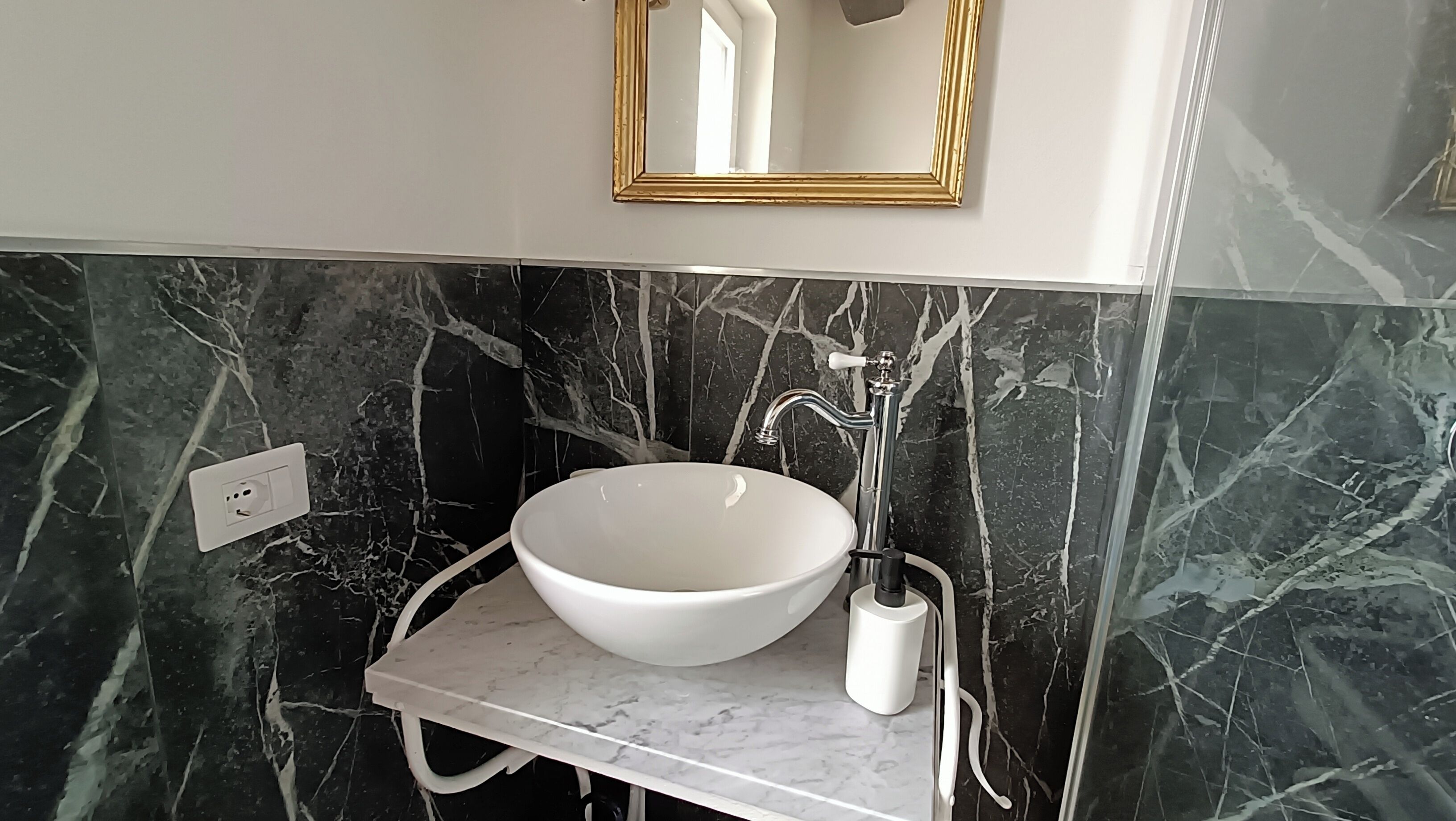 A bathroom with a white sink, a gold-framed mirror, and black marble walls.