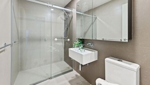 Uma casa de banho moderna com chuveiro em cabine de vidro, lavatório branco e sanita.