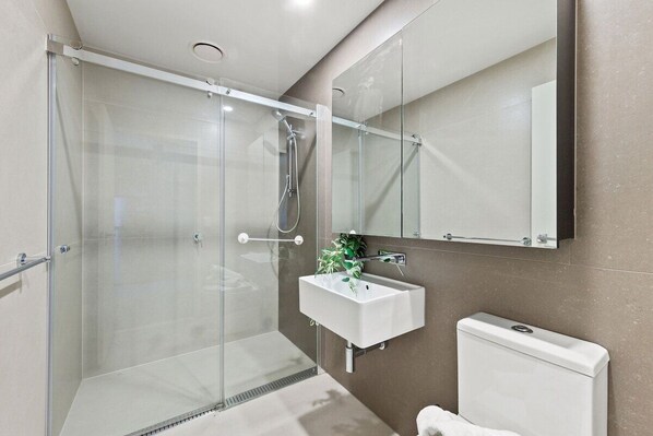 A modern bathroom with a glass-enclosed shower, a white sink, and a toilet.