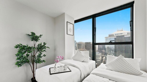 Quarto de hotel moderno com duas camas, uma janela grande, vista para a cidade e um vaso de planta.