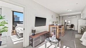 Quarto de hotel moderno com cama, escrivaninha, televisão, cozinha compacta e varanda com vista para a cidade.
