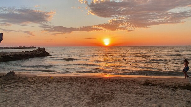 Une plage au coucher du soleil, avec une côte rocheuse et une personne qui se promène.