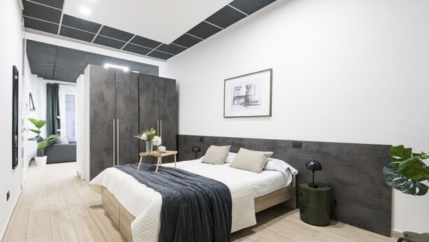 Un dormitorio moderno con cama, mesita de noche, lámpara y un cuadro enmarcado en la pared.