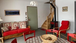 Een gezellige woonkamer met een bank, rode stoelen, een tafel met een mand, een houten trap en een open haard.