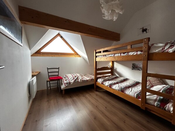 A dormitory room with bunk beds, a desk, and a chair.