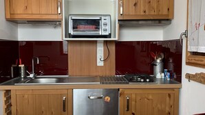 Een kleine keuken met houten kastjes, een ingebouwde magnetron en een roestvrijstalen koelkast.