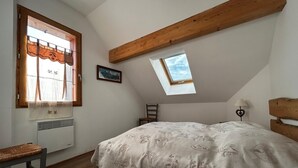 Een slaapkamer met een schuine hemel, dakraam, bed met een beddengoed met een patroon, een stoel, een nachtkastje en een foto aan de muur.
