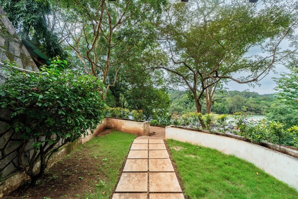 A stone pathway leading through a lush garden with a view of a river and distant hills. - Bison River Resort Dandeli (Joida)