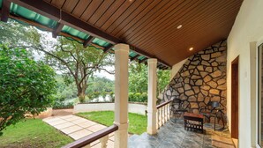 A covered outdoor area with stone walls, a wooden ceiling, and a seating area with chairs and a bench. - Bison River Resort Dandeli (Joida)
