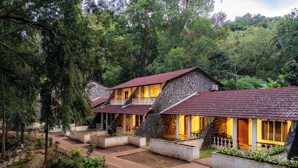 A row of stone buildings with red-tiled roofs, surrounded by lush greenery. - Bison River Resort Dandeli (Joida)