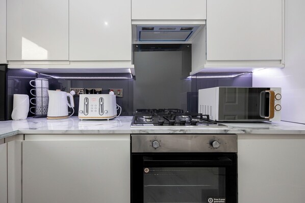 Une cuisine moderne avec des meubles blancs, une cuisinière à gaz, un four à micro-ondes, un grille-pain et un lave-vaisselle.