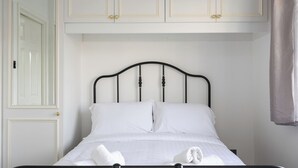 Una cama con sábanas y toallas blancas, cabecera de metal negro y armarios blancos arriba.