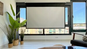 Una sala de estar moderna con un televisor de pantalla plana grande montado en la pared, una mesa de centro de madera, un sofá negro y plantas en macetas.