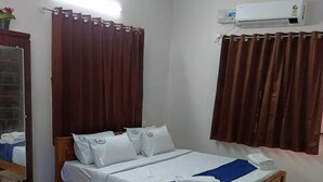 A bedroom with a wooden bed, white bedding, a blue bed runner, a wooden nightstand, a mirror, a ceiling fan, and an air conditioning unit. - Rithu's inn (Tirupattur)