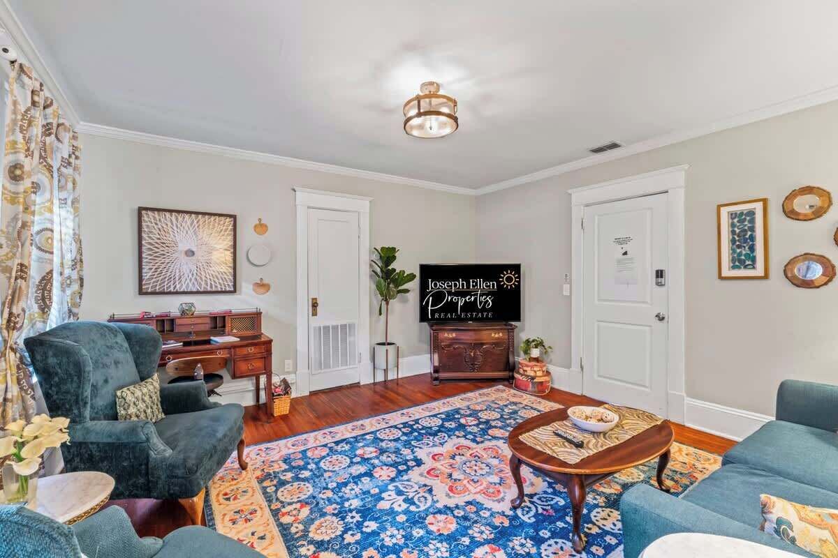 A living room with a blue sofa, a patterned rug, a wooden coffee table, a TV, and a sign that reads 'Joseph Ellen Properties Real Estate'.