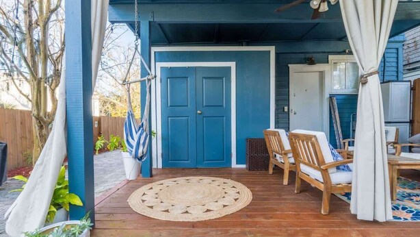 Eine überdachte Veranda mit einer blauen Tür, Holzstühlen, einem gewebten Teppich und einem Deckenventilator.