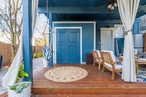 A covered porch with a blue door, wooden chairs, a woven rug, and a ceiling fan. - Bohemian Riverside - Team Joseph Ellen (Jacksonville)
