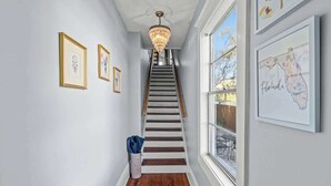 Eine Treppe mit einer Chandelüstere, gerahmte Kunstwerke an den Wänden und ein Fenster mit Gartenmöbeln.