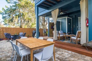 Een terras buiten met een houten tafel en witte stoelen, een overdekt zitgedeelte met stoelen en een tafel, en een houten omheining.