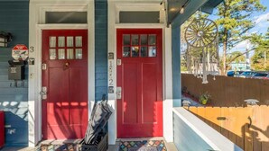 Une maison à deux étages avec une porte rouge, un paillasson et un panneau indiquant la présence d’un système de sécurité.