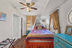 Een slaapkamer met een bed, een plafondventilator, een raam met gordijnen en een dressoir.