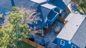 Un barrio residencial con una casa azul, un patio con mobiliario exterior y un árbol.