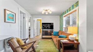 A living room with a sofa, a chair, a TV, and a sign for Joseph Ellen Properties Real Estate. - Mid-Century Modern Riverside - Team Joseph Ellen (Jacksonville)