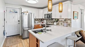 A modern kitchen with white cabinets, stainless steel appliances, a central island with bar seating, and pendant lighting. - Mid-Century Modern Riverside - Team Joseph Ellen (Jacksonville)